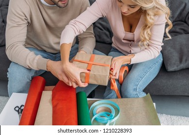 Cropped Image Of Couple Wrapping Christmas Gift Box Together At Home