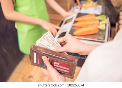 Cropped Image Of A Customer Holding Money To Pay His Buy On The Foreground 