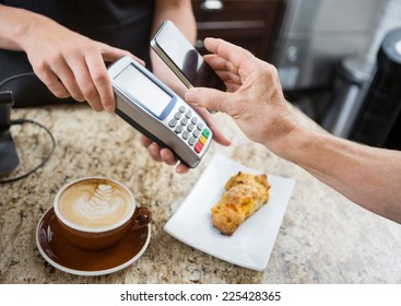 Cropped image of customer paying through mobilephone over electronic reader at cafe counter - Powered by Shutterstock