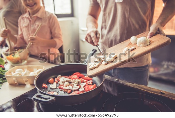 Cropped image of cute little\
girl and her beautiful parents cooking together in kitchen at\
home