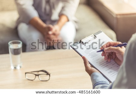 Cropped image of depressed man at the psychotherapist. Doctor is making notes while listening to his patient