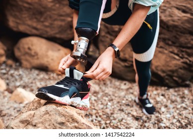 Cropped image of disabled athlete young woman in sports clothing with prosthetic leg tying shoelace while standing at the beach - Powered by Shutterstock
