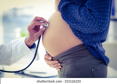Cropped image of doctor using stethoscope white examining pregnant woman in clinic