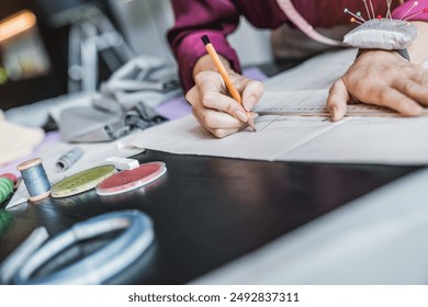 Cropped image of fashion designer woman working drawing her new design on a paper in her workshop. Female tailor hands draw sew pattern, ruler threads and needles on the table - Powered by Shutterstock