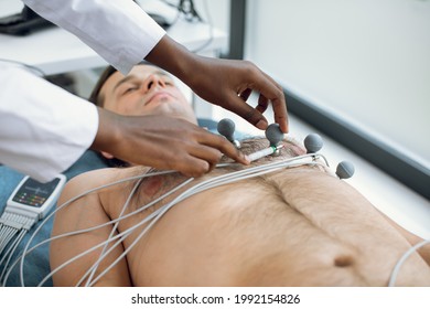 Cropped Image Of Female African American Doctor Or Nurse Sticking Holter And Vacuum Electrodes On Young Male Patient's Chest In Hospital. ECG And Heart Health Concept. Annual Health Check