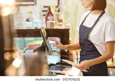 Cropped image of female barista working at coffeeshop and using cash register when accepting payment or entering order detaikls