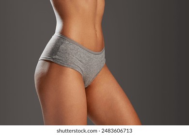 Cropped image of female body in underwear, girl with slim waist and fit buttocks against grey studio background. Concept of female beauty, body and skin care, fitness, wellness, diet