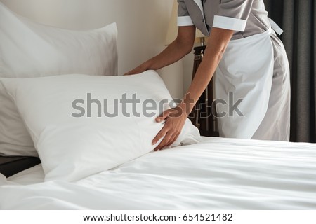 Cropped image of a female chambermaid making bed in hotel room