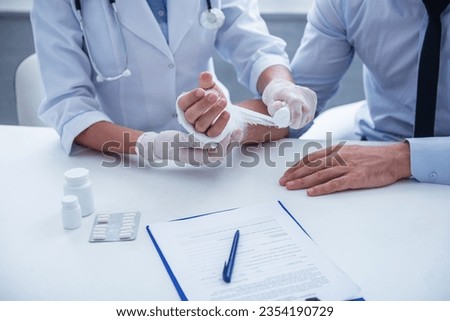 Cropped image of female doctor bandaging man's damaged hand while working in her office