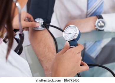 Cropped image of female doctor checking businessman's blood pressure in clinic