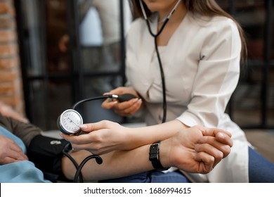 Cropped Image. Female Doctor Measuring Blood Pressure To Older Patient Sitting At Sofa.