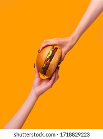 cropped image of female hands holding burger against yellow background