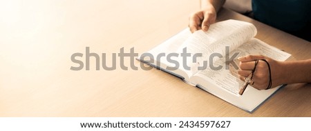 Cropped image of female reading a bible book while holding cross at wooden table with blurring background. Concept of hope, religion, faith, christianity and god blessing. Warm. Burgeoning.