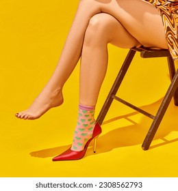 Cropped image of female slender legs on heeled shoe and funny socks against bright yellow background. Concept of pop art photography, creative vision, imagination, sales, fashion, style