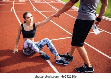 Cropped Image Of A Fitness Man With Water Bottle Helping Young Girl To Get Up At The Stadium