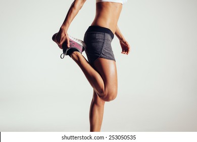 Cropped Image Of A Fitness Woman Stretching Her Legs Against Grey Background.  Fit Female Runner Doing Stretches.