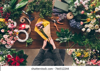 cropped image of florist wrapping bouquet in pack paper in shop