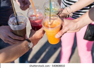 Cropped image of friends in casual clothing having a toast holding various fruit smoothies in plastic cups with straws together. Sunny day - Powered by Shutterstock