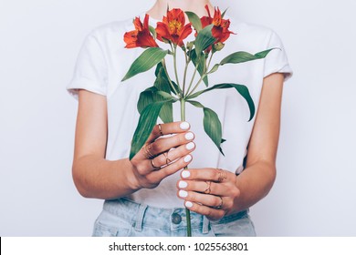 Cropped image of a girl in jeans and a T-shirt holding a red flower in her hands with a manicure on a white background - Powered by Shutterstock