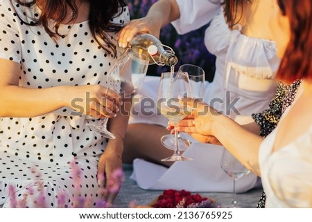 Cropped image of girlfriends pouring white wine in glasses at nature outdoor at sunny summer day. Close up. Banner for website.