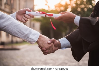 Cropped image of graduate in academic dress taking his diplomas and shaking hand - Shutterstock ID 734610241