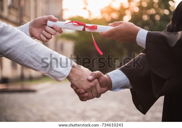 Cropped image of graduate in academic dress taking\
his diplomas and shaking\
hand