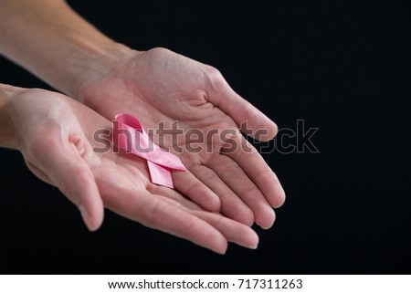Cropped image of hands holding pink ribbon against black background