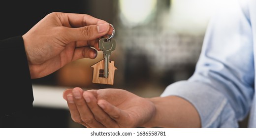 Cropped image Hands of real estate agent offering/giving a house key to smart man in blue shirt while standing together over modern bank as background. Broker/Seller/Dealer concept. - Shutterstock ID 1686558781
