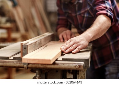 Cropped image of the hands of a skilled craftsman cutting a wooden plank with a circular saw in a workshop