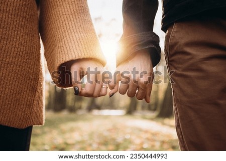 Cropped image hands young loving couple pinky swear, pinky promise hook each other's little finger, hugging smiling kissing laughing spending time together. Autumn, fall season, maple leaves
