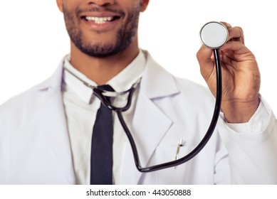 Cropped image of handsome Afro American doctor in white coat smiling while holding a stethoscope, isolated on white background