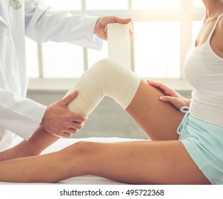 Cropped Image Of Handsome Doctor Bandaging Woman's Injured Knee While Working In His Office