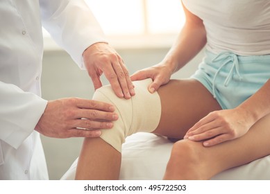 Cropped image of handsome doctor bandaging woman's injured knee while working in his office