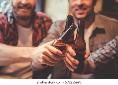Cropped image of handsome friends clinking bottles of beer and smiling while resting at the pub - Powered by Shutterstock