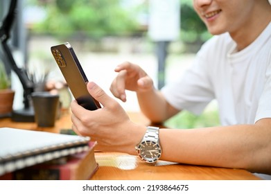 cropped image, A handsome guy using his smartphone, touching on phone screen, typing on chat, texting with his friends.