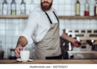 Cropped image of handsome male barista is working in coffee shop. Bearded man behind the bar counter is making coffee.