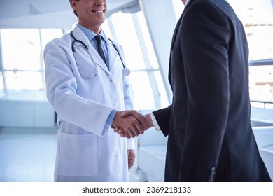 Cropped image of handsome mature doctor and young businessman shaking hands while standing in the hospital hall - Powered by Shutterstock