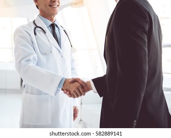 Cropped image of handsome mature doctor and young businessman shaking hands while standing in the hospital hall - Powered by Shutterstock