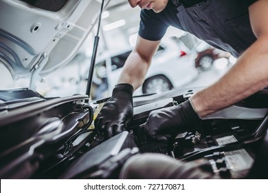 Cropped image of handsome mechanic in uniform is working in auto service. Car repair and maintenance.