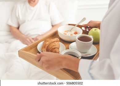 Cropped image of handsome old patient getting his meal from nurse while lying in bed in hospital - Powered by Shutterstock