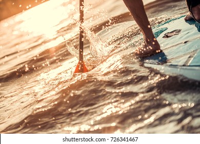 Cropped image of handsome young man SUP surfing on the river, sun is going down