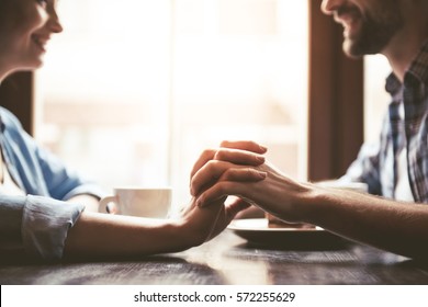 Cropped image of happy young couple holding hands, looking at each other and smiling while sitting at the cafe - Powered by Shutterstock