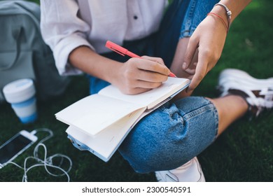 Cropped image of intelligent female student writing information in education textbook while doing homework test, unrecognizable clever woman with pen and notepad studying and learning in city