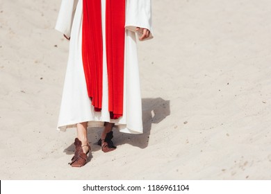 Cropped Image Of Jesus In Robe, Red Sash And Sandals Walking On Sand In Desert