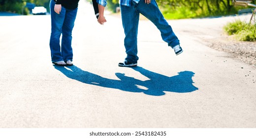 Cropped image of the legs of a couple standing together in the road and leaning together to for a kiss. You can see their kiss in the shadows.  - Powered by Shutterstock