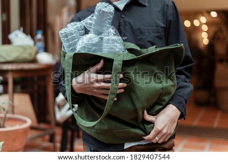 Cropped image of lots of plastic bottle in the green canvas bag in the man's arms.