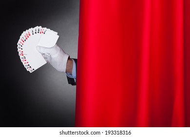 Cropped Image Of Magician Holding Fanned Cards Behind Stage Curtain