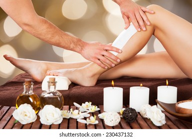 Cropped Image Of Male Beautician Waxing Woman's Leg In Spa