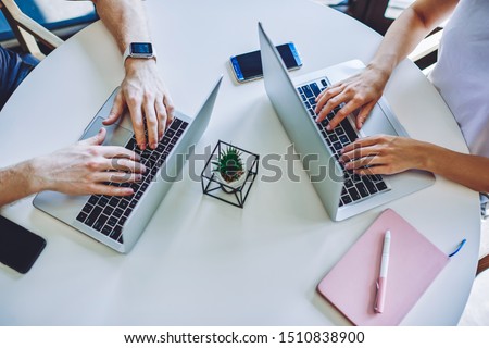 Cropped image of male and female hands typing text article for posting content on website using free wireless 4g internet in coworking space, it professionals updating software on laptop computers
