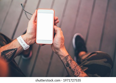 Cropped image of male hands with stylish tattoo holding cellular gadget with blank screen area for your internet advertising, millennial guy using smartphone device with mock up for checking email